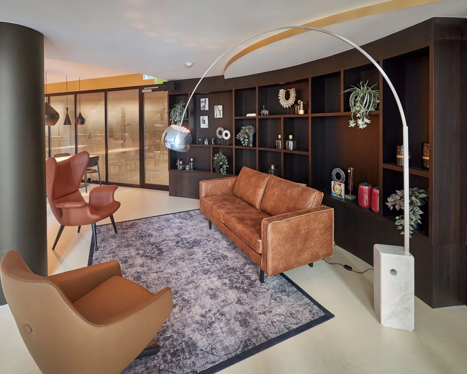 Modern ingerichte loungehoek met leren meubels, wandkast en booglamp in een kantoorruimte.