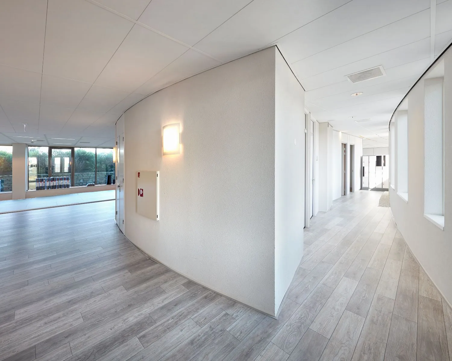 Moderne, lichte gang met houten vloer en gebogen muren in een kantoorgebouw of zorginstelling.