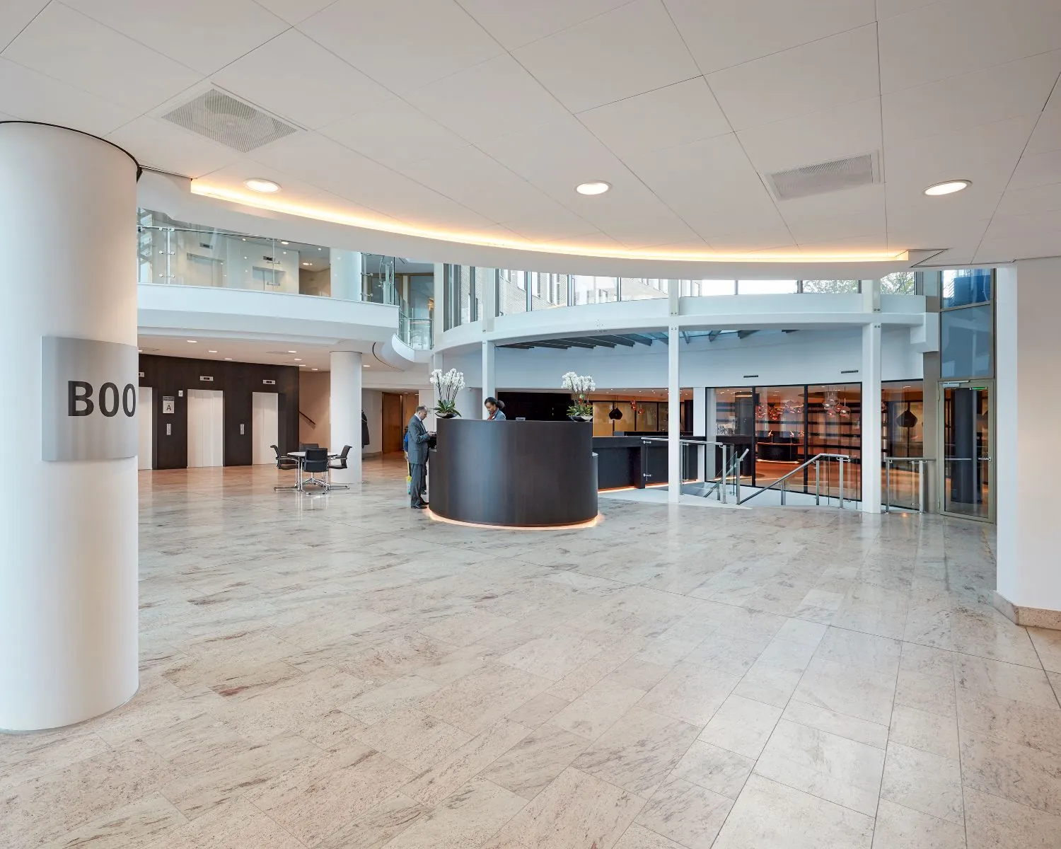 Moderne en lichte kantoorlobby met een ronde receptiebalie, marmeren vloer en liften op de achtergrond.