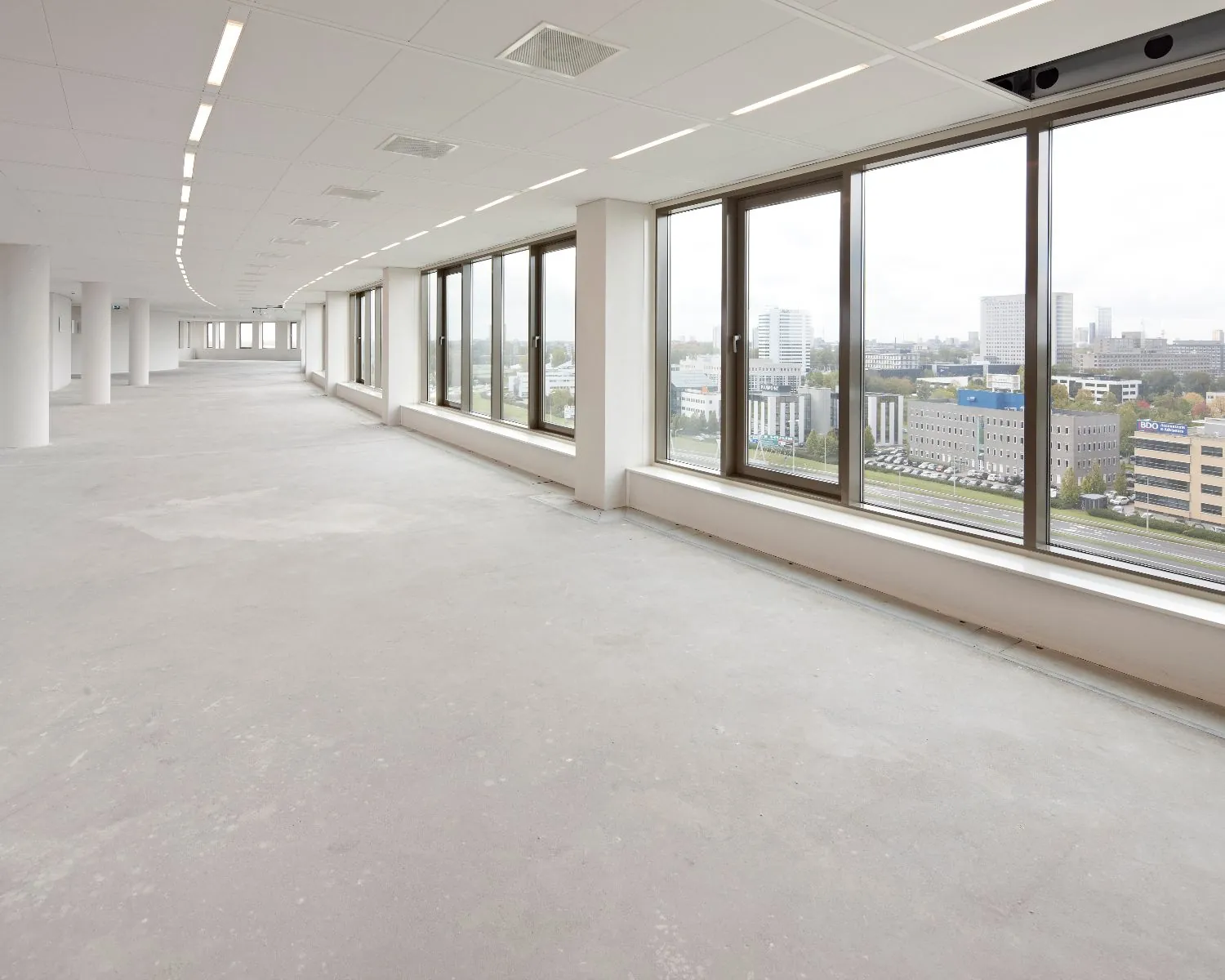 Lege, lichte kantoorruimte met grote ramen en uitzicht op een stedelijk zakendistrict.