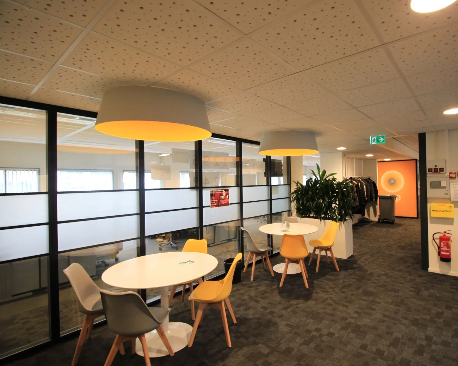 Moderne kantoorlounge met ronde tafels, gekleurde stoelen en grote hanglampen.