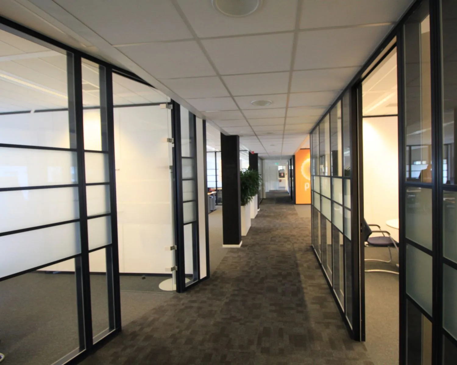 Moderne kantoorruimte met glazen vergaderruimtes en een brede gang met tapijtvloer.
