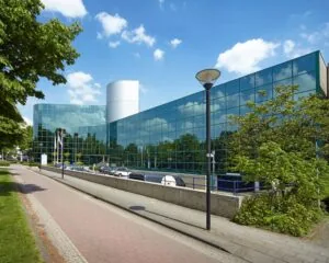 Modern glazen kantoorgebouw met spiegelende ramen aan een rustige straat op een zonnige dag.