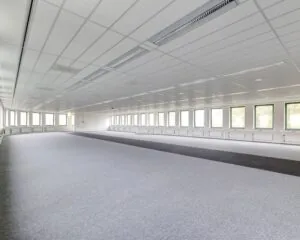 Lege, ruime kantoorruimte met tapijtvloer en een rij ramen langs beide zijden.