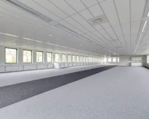 Grote lege kantoorruimte met grijze vloerbedekking, meerdere ramen en systeemplafond met verlichting.