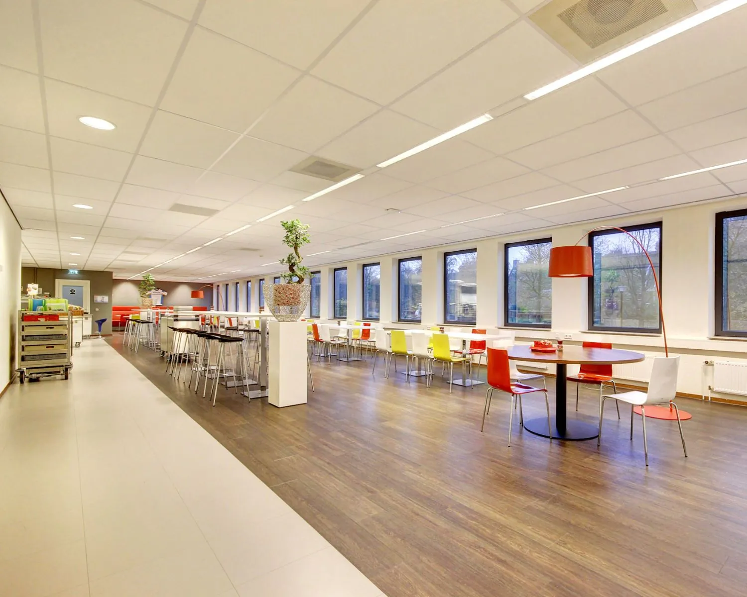 Moderne, kleurrijk ingerichte bedrijfskantine met grote ramen en diverse zitmogelijkheden.