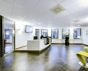 Moderne en lichte receptieruimte met strakke balie, zwarte vloertegels en meerdere grote ramen.