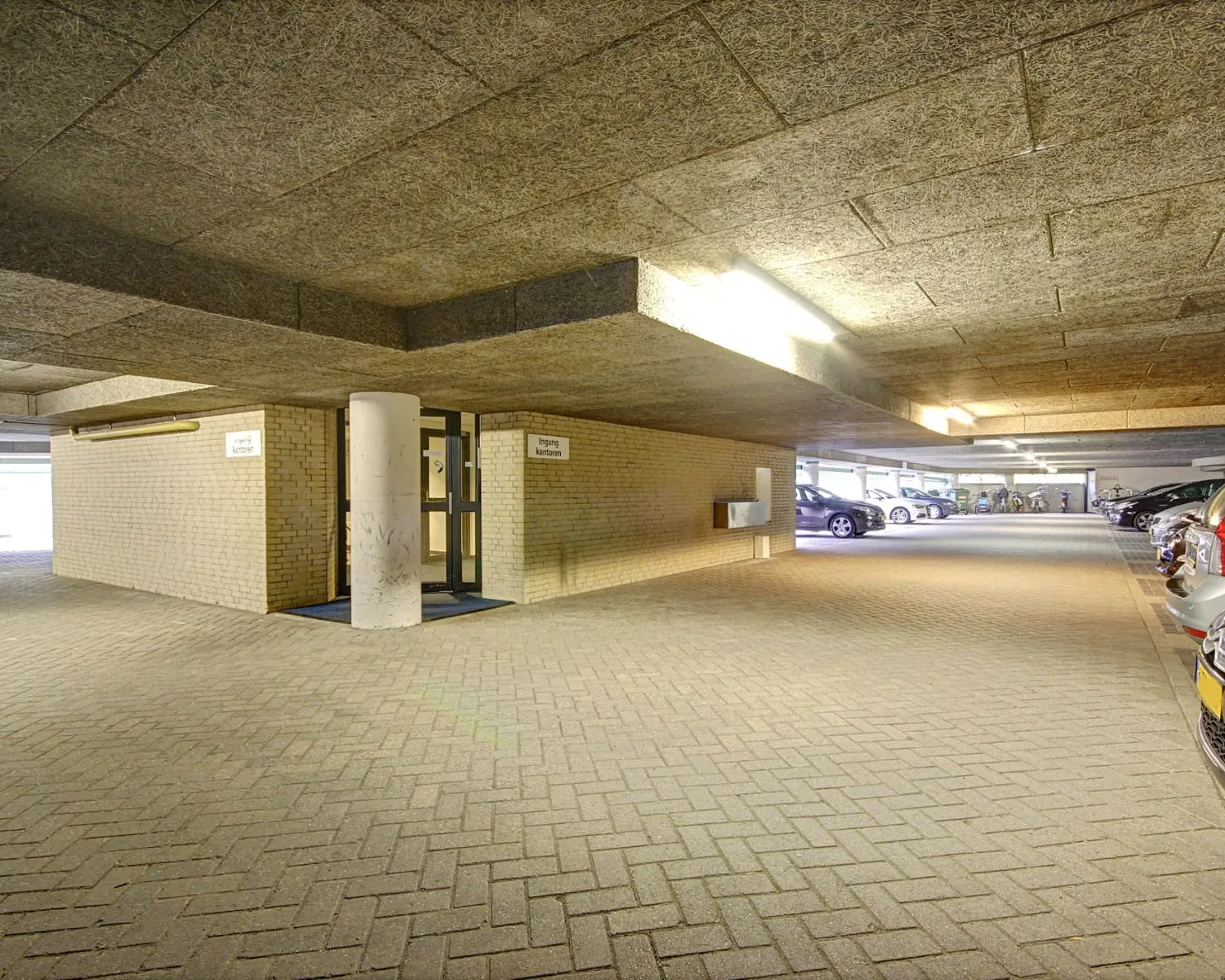 Overdekte parkeergarage met een ingang naar kantoren en geparkeerde auto's langs de zijkant.