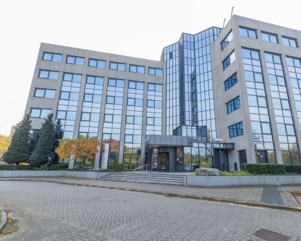 Zakelijk kantoorgebouw met glazen gevel en betonnen elementen, gezien vanaf de ingang.