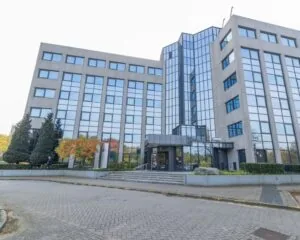 Zakelijk kantoorgebouw met glazen gevel en betonnen elementen, gezien vanaf de ingang.