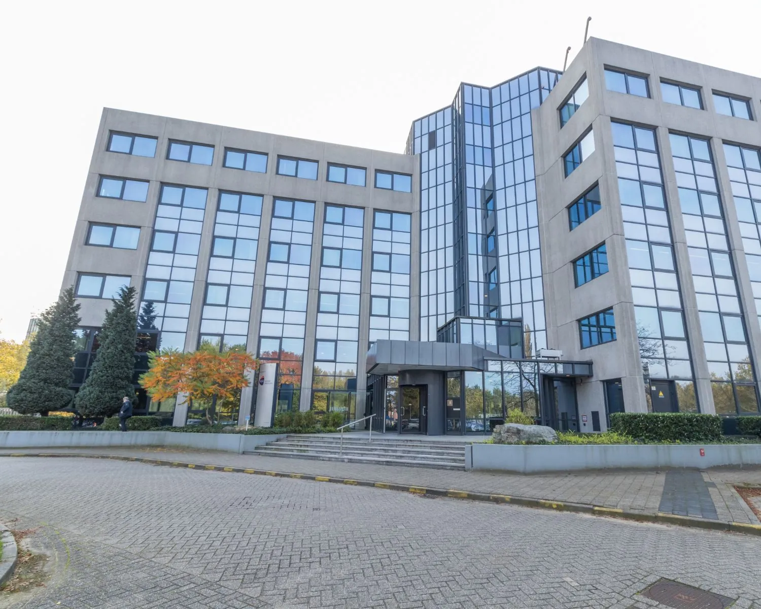 Zakelijk kantoorgebouw met glazen gevel en betonnen elementen, gezien vanaf de ingang.