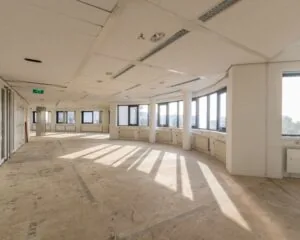 Leegstaand kantoorpand met grote ramen en zichtbaar onafgewerkte vloer.