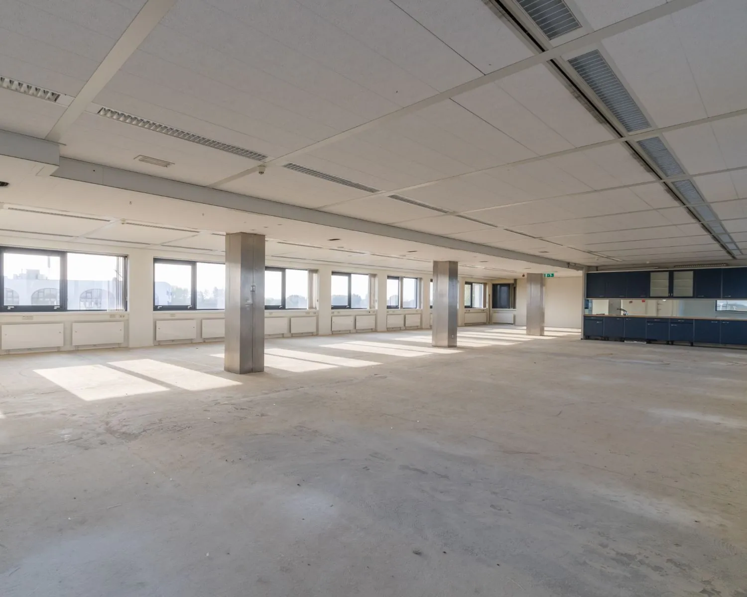 Leeg, ruim en licht kantoorinterieur met grote ramen en systeemplafond.