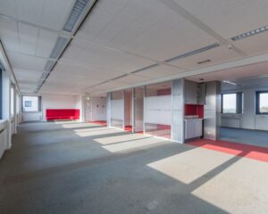 Licht en ruim leegstaand kantoorpand met glazen scheidingswanden en rode accenten.