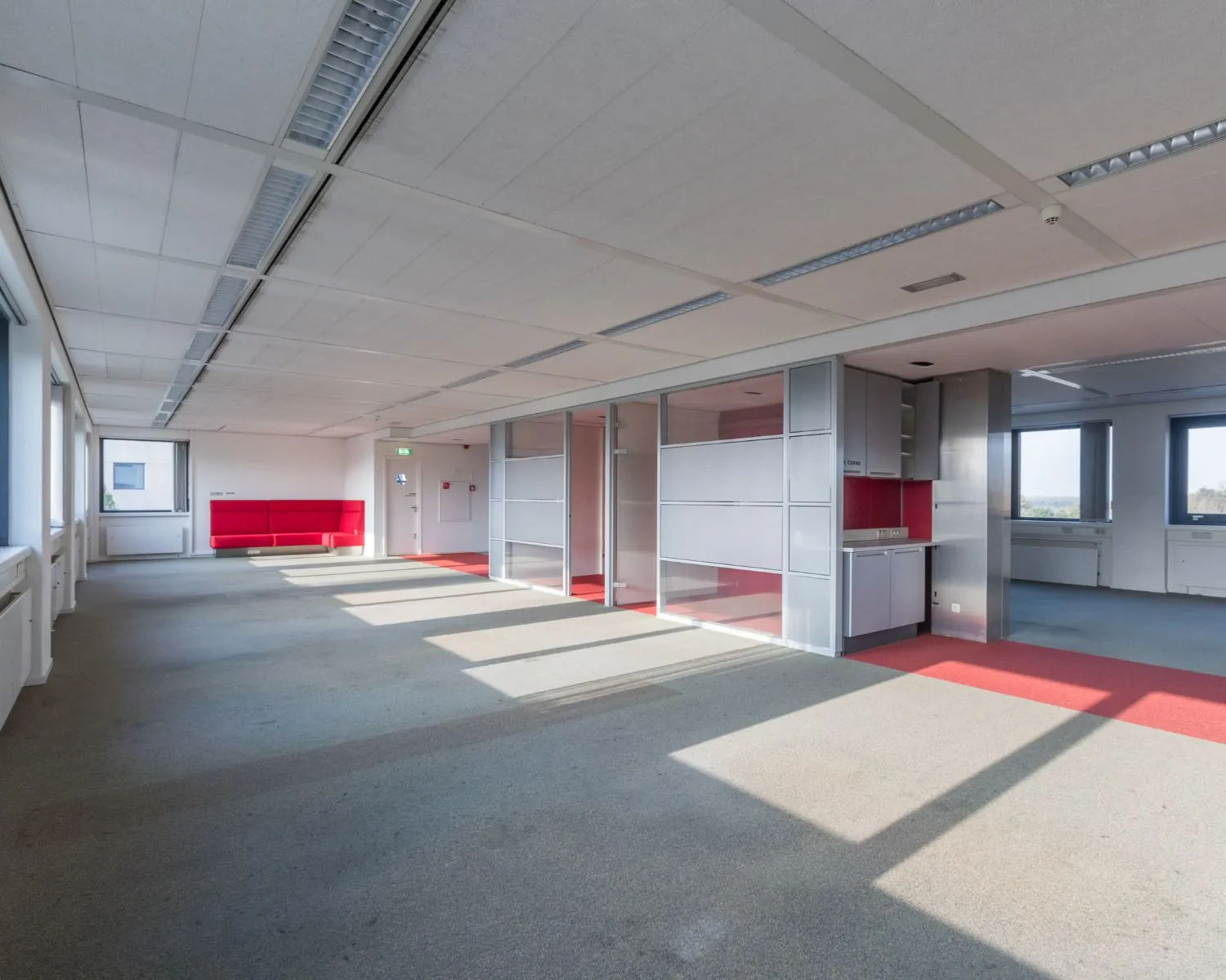 Licht en ruim leegstaand kantoorpand met glazen scheidingswanden en rode accenten.