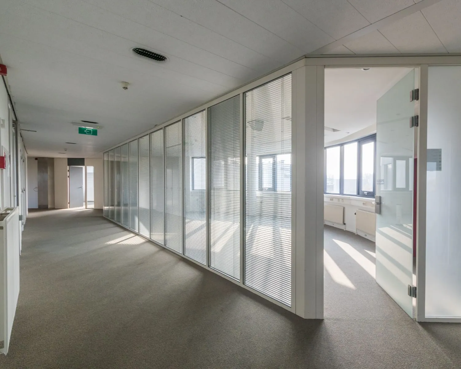 Lichte, moderne kantoorruimte met glazen scheidingswanden en openstaande deur naar een vergaderruimte.