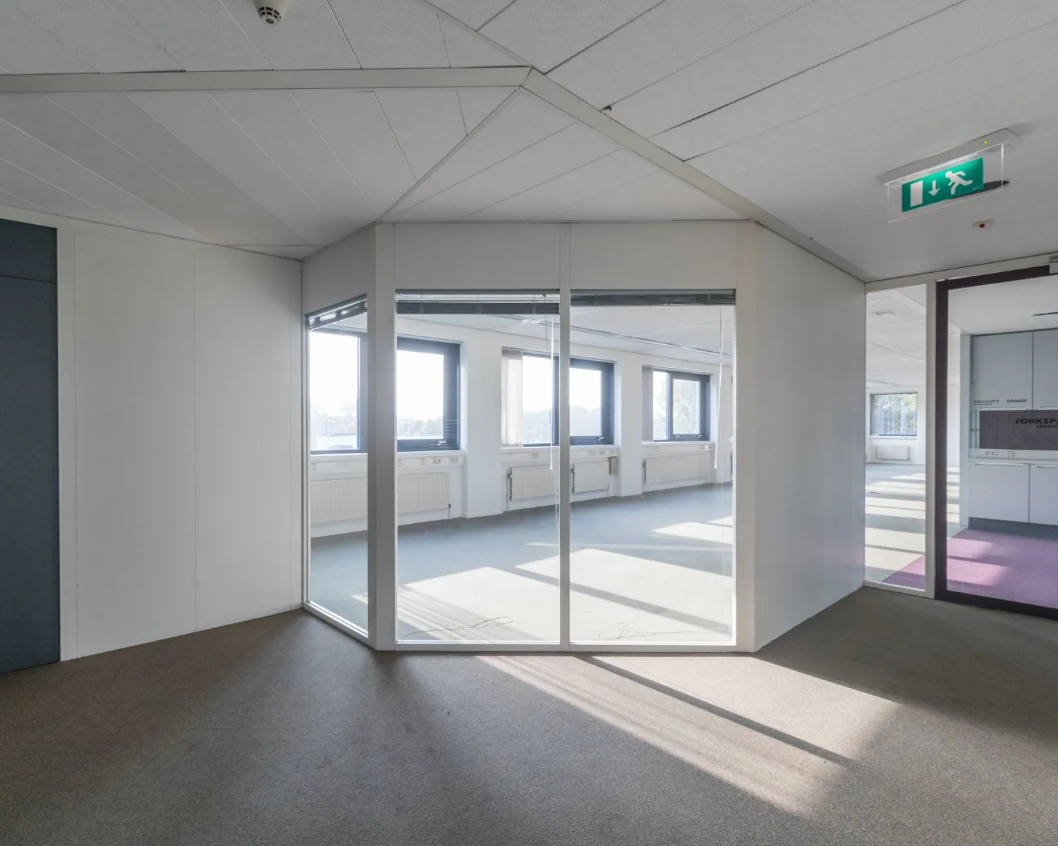 Lichte, moderne kantoorruimte met glazen tussenwand en grote ramen.