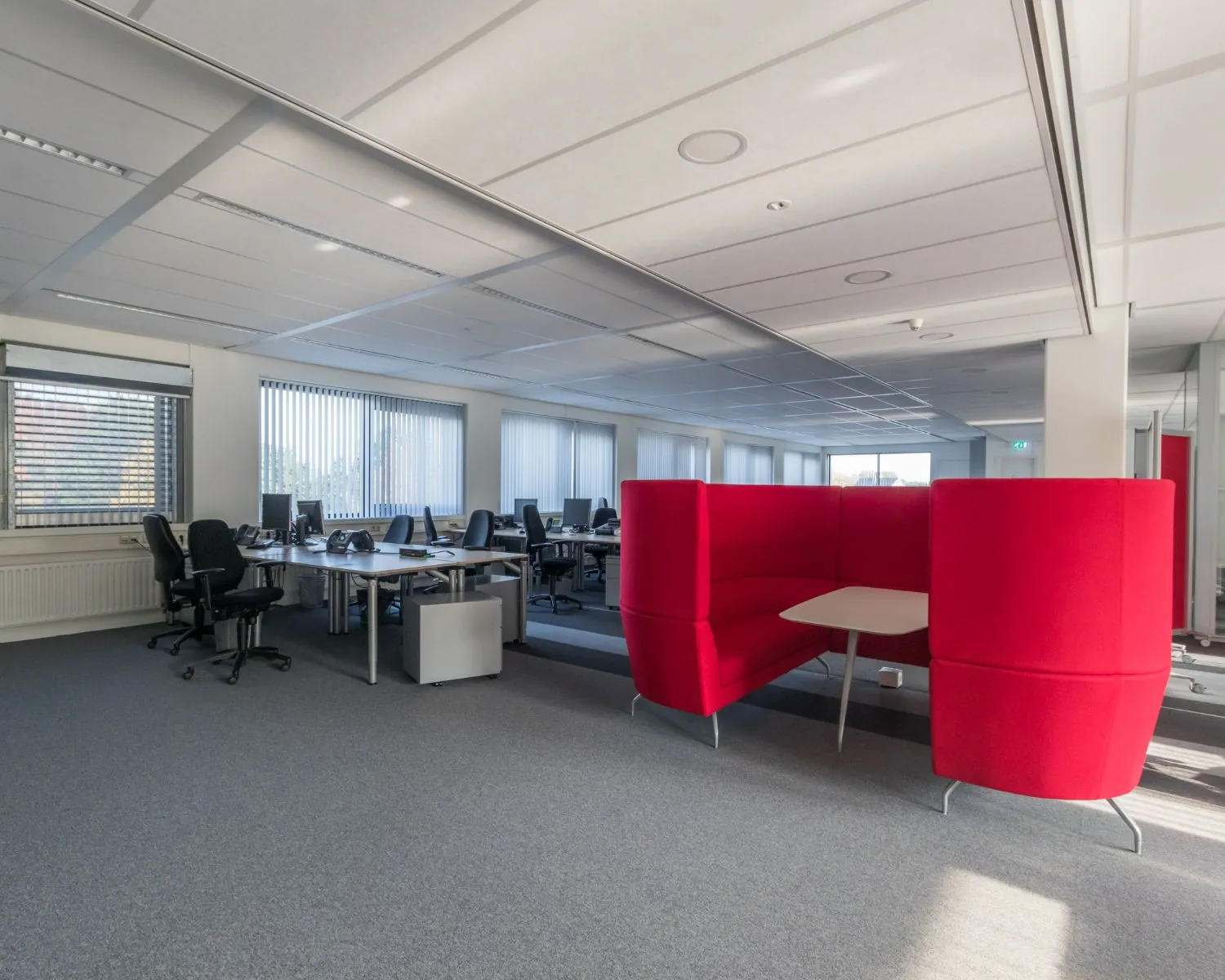 Modern kantoor met open werkplekken en een opvallende rode overlegzit met tafel.
