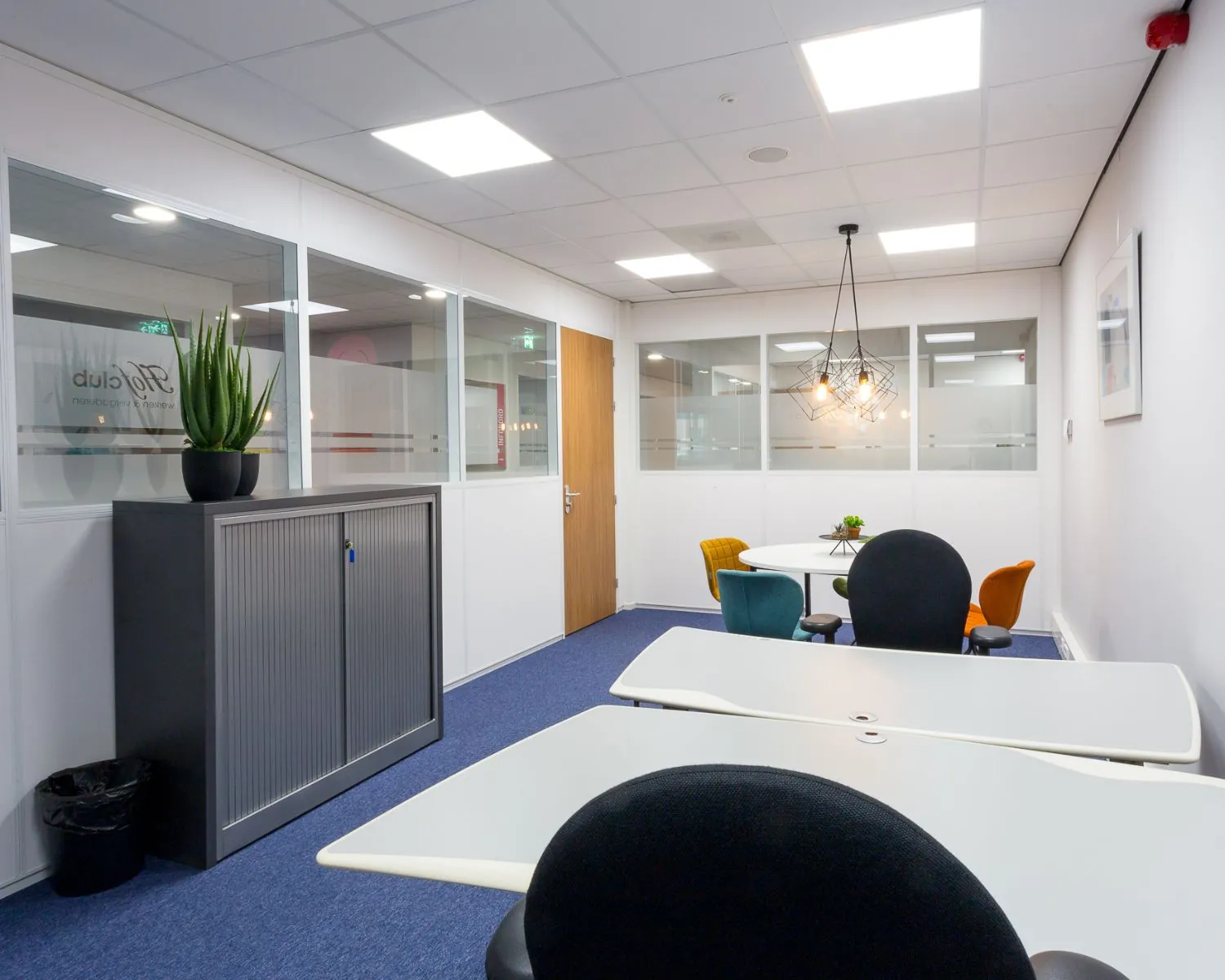 Moderne en kleurrijke kantoorruimte met werkplekken, vergadertafel en hanglamp.