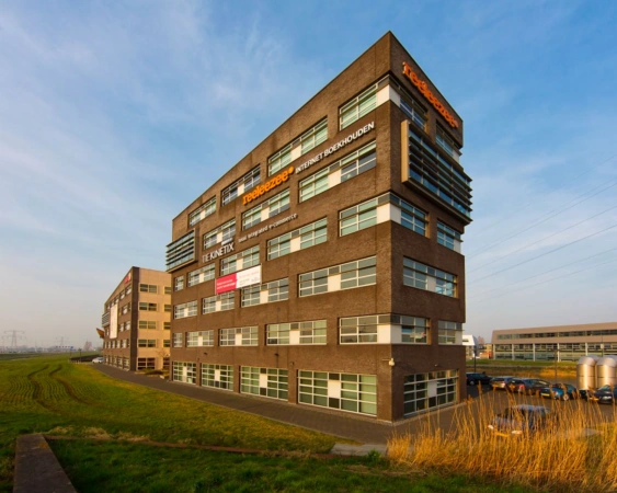 Modern kantoorgebouw met het logo van Teejeezee en andere bedrijven, gelegen aan een grasveld onder een heldere lucht.