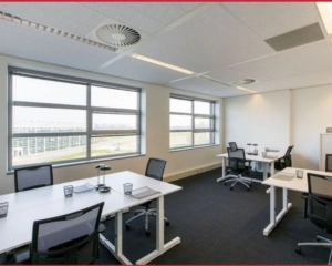 Modern, licht kantoor met vier werkplekken, grote ramen en ergonomische bureaustoelen.