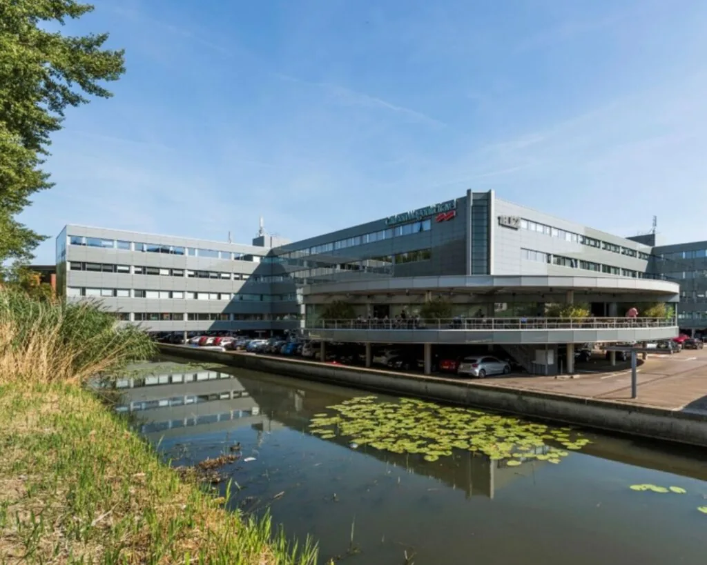 Kantoorgebouw "Croped_1557906213" met parkeergarage aan een vijver met waterlelies op een zonnige dag.
