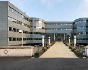 Modern kantoorgebouw met glazen gevel en een toegangsbrug versierd met lantaarns en plantenbakken.