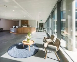 Moderne en lichte wachtruimte met comfortabele stoelen, een ronde tafel met bloemen en een houten receptiebalie.