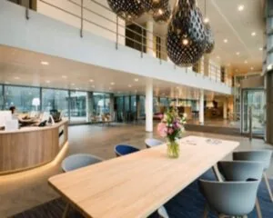Moderne kantoorlobby met houten receptiebalie, designverlichting en een tafel met bloemen in een vaas.