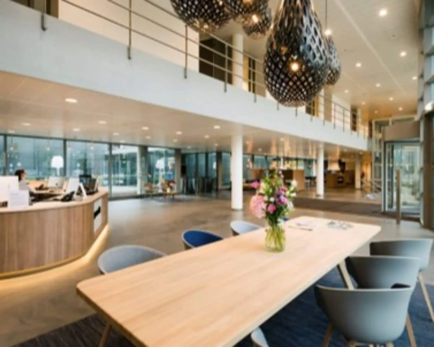 Moderne kantoorlobby met houten receptiebalie, designverlichting en een tafel met bloemen in een vaas.