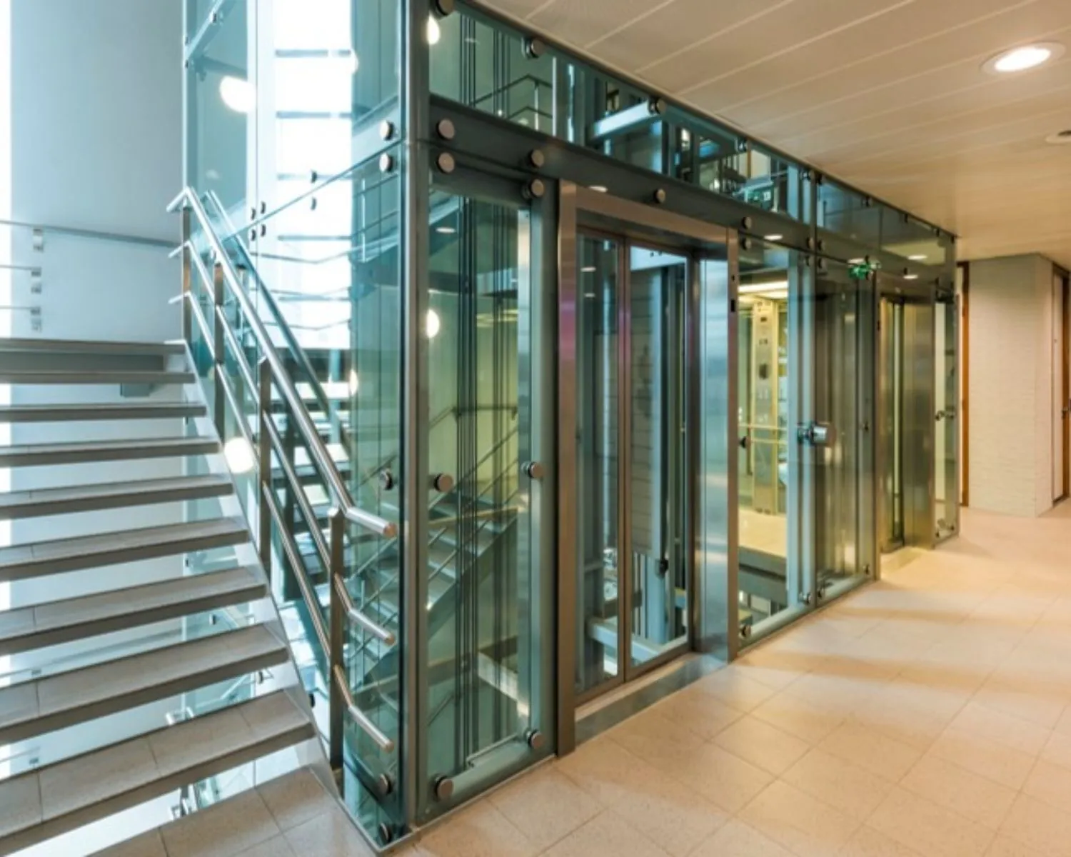 Moderne glazen lift en trap in een kantoorgebouw met metalen afwerking.
