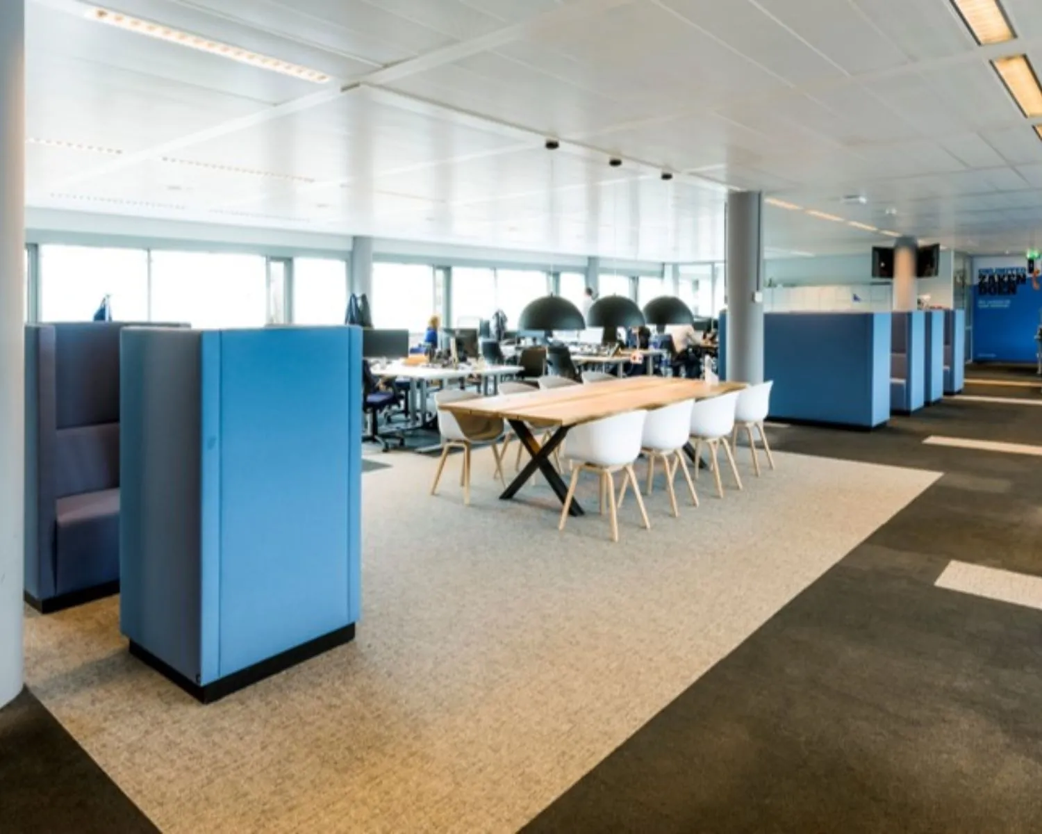Moderne open kantoorruimte met flexibele werkplekken, vergadertafel en akoestische zitunits.