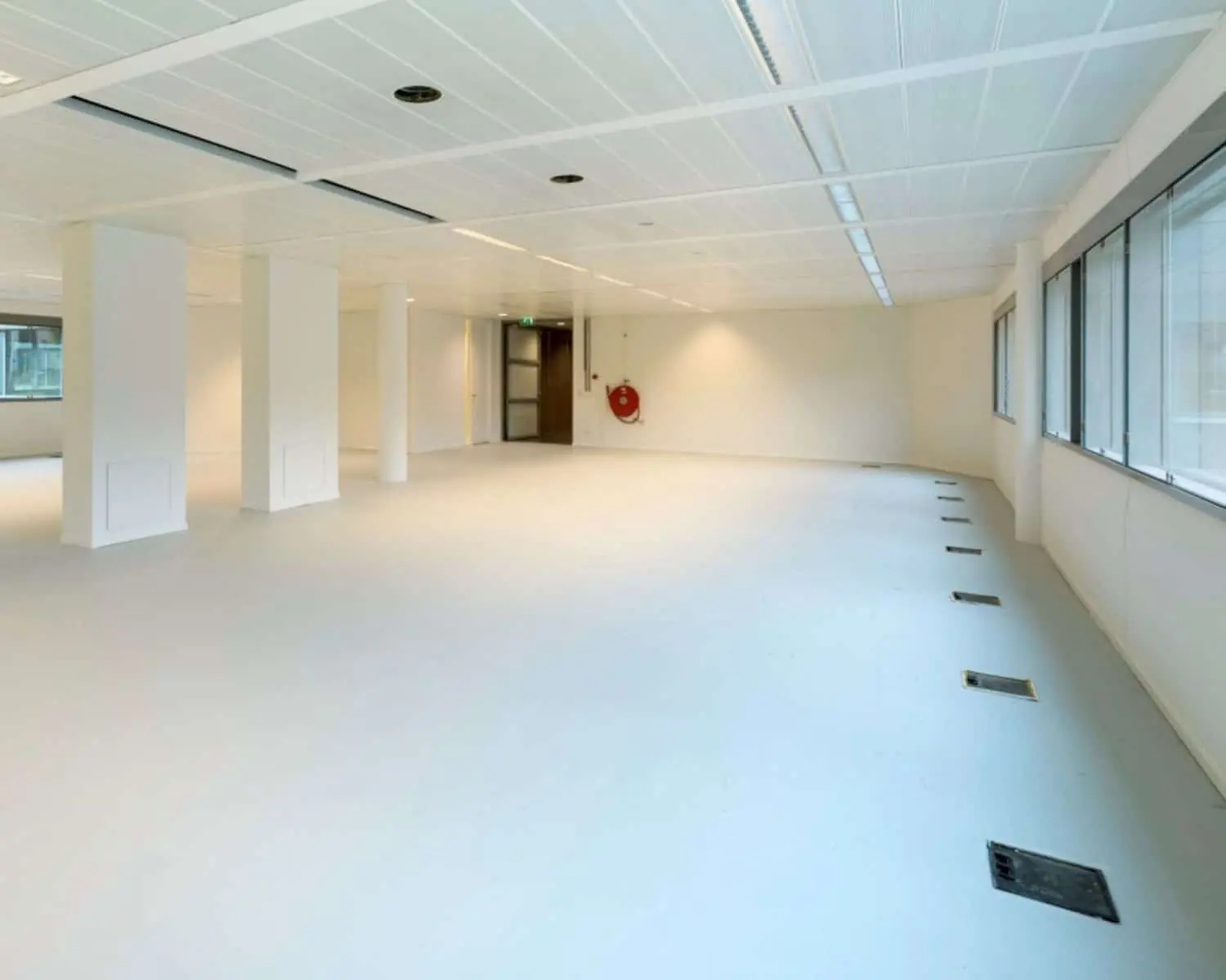 Leeg, modern kantoorpand met witte muren, kolommen en grote ramen aan één zijde.