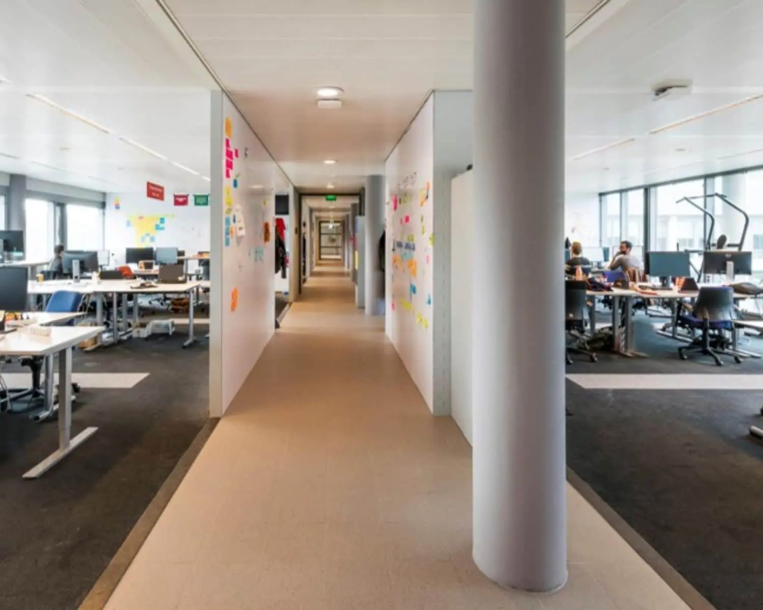 Open kantooruimte met werkplekken aan weerszijden van een centrale gang en kleurrijke post-its op de muren.