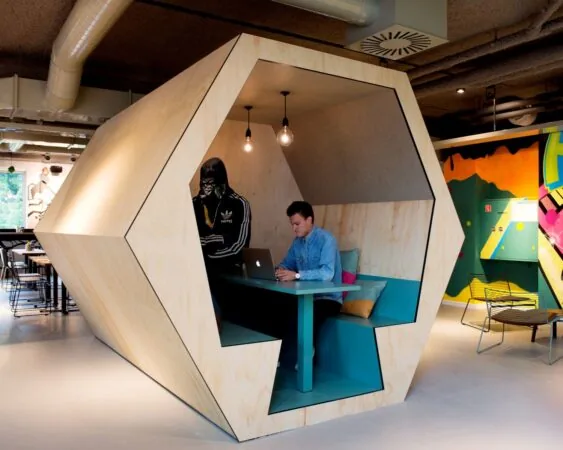 Man werkt op laptop in moderne houten werkcabine met opvallende muurschildering op de achtergrond.