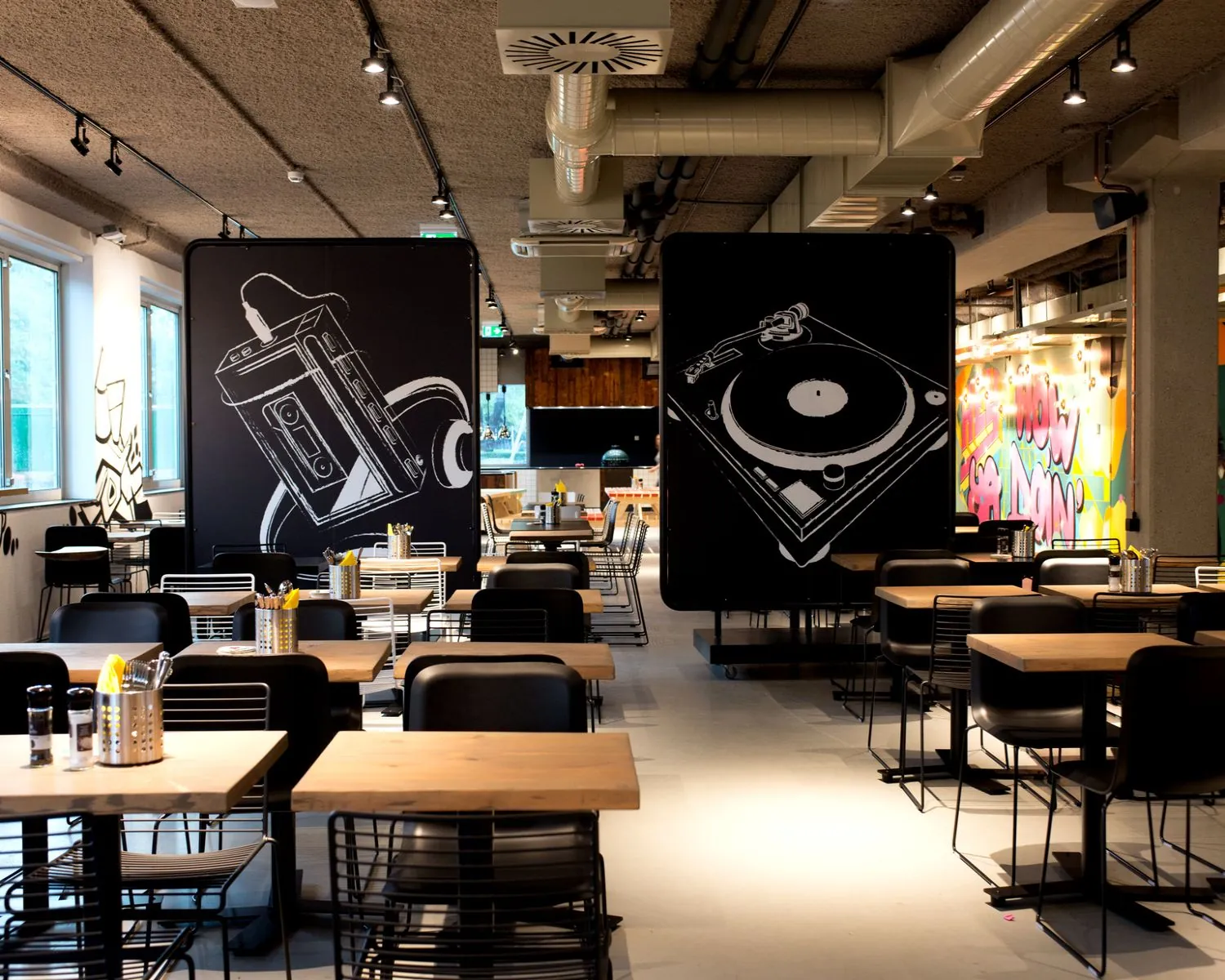 Modern ingerichte eetzaal met zwarte muurschermen waarop een cassettebandje met koptelefoon en een platenspeler zijn afgebeeld.