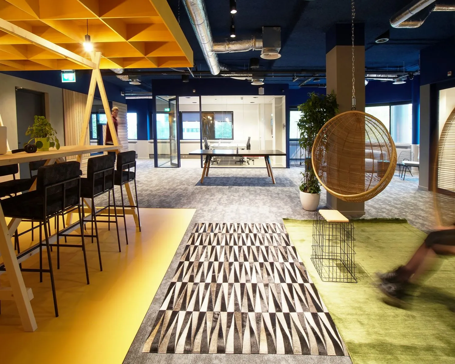 Modern ingerichte kantooruimte met kleurrijke accenten, hangstoel en open werkplekken.