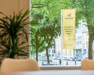 Uitzicht vanuit een vergaderruimte op een straat met een gele StartDock-vlag voor co-working en vergaderruimtes.