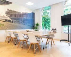 Moderne vergaderruimte met witte stoelen, een houten tafel en een grote muurfoto van een schip aan de kade.