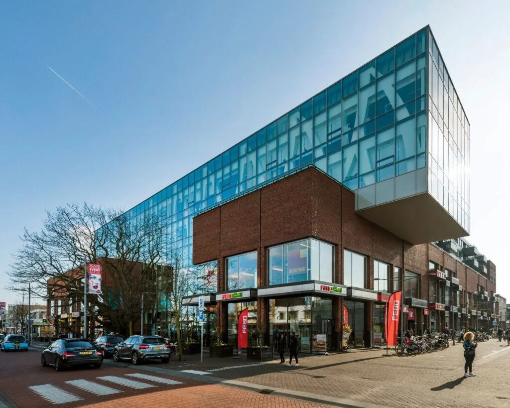 Modern winkel- en kantoorpand met glazen bovenverdieping en winkels zoals FEBO en Scapino aan een drukbezochte straat.