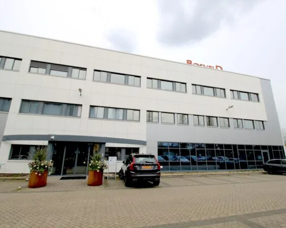 Vooraanzicht van een modern kantoorpand met de naam "Bosveld" op het dak en geparkeerde auto's voor de ingang.