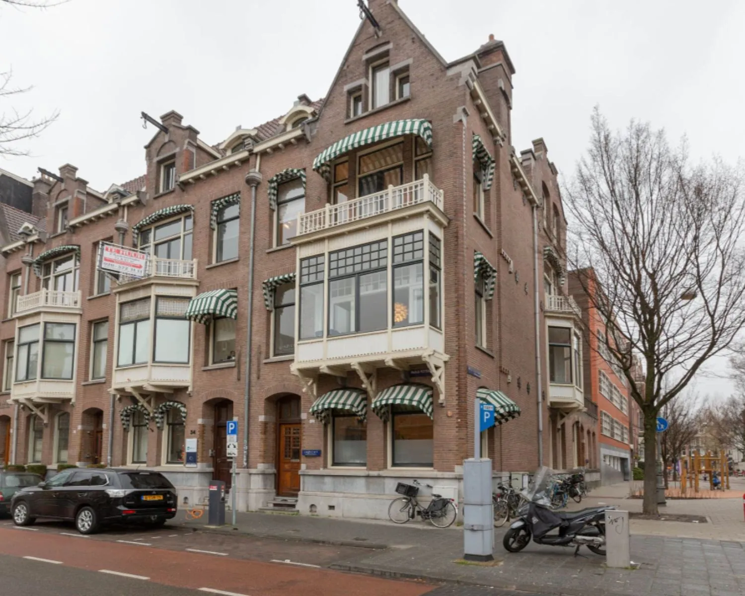 Rij karakteristieke herenhuizen met groen-wit gestreepte markiezen aan een Amsterdamse straat.