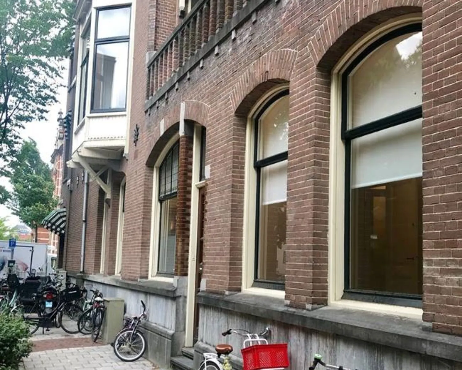 Bakstenen gevel van een oud pand met hoge ramen en geparkeerde fietsen op de stoep.