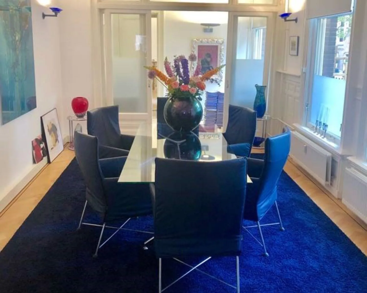 Moderne vergaderruimte met een glazen tafel, zes zwarte stoelen en een bloemenvaas op een donkerblauw tapijt.