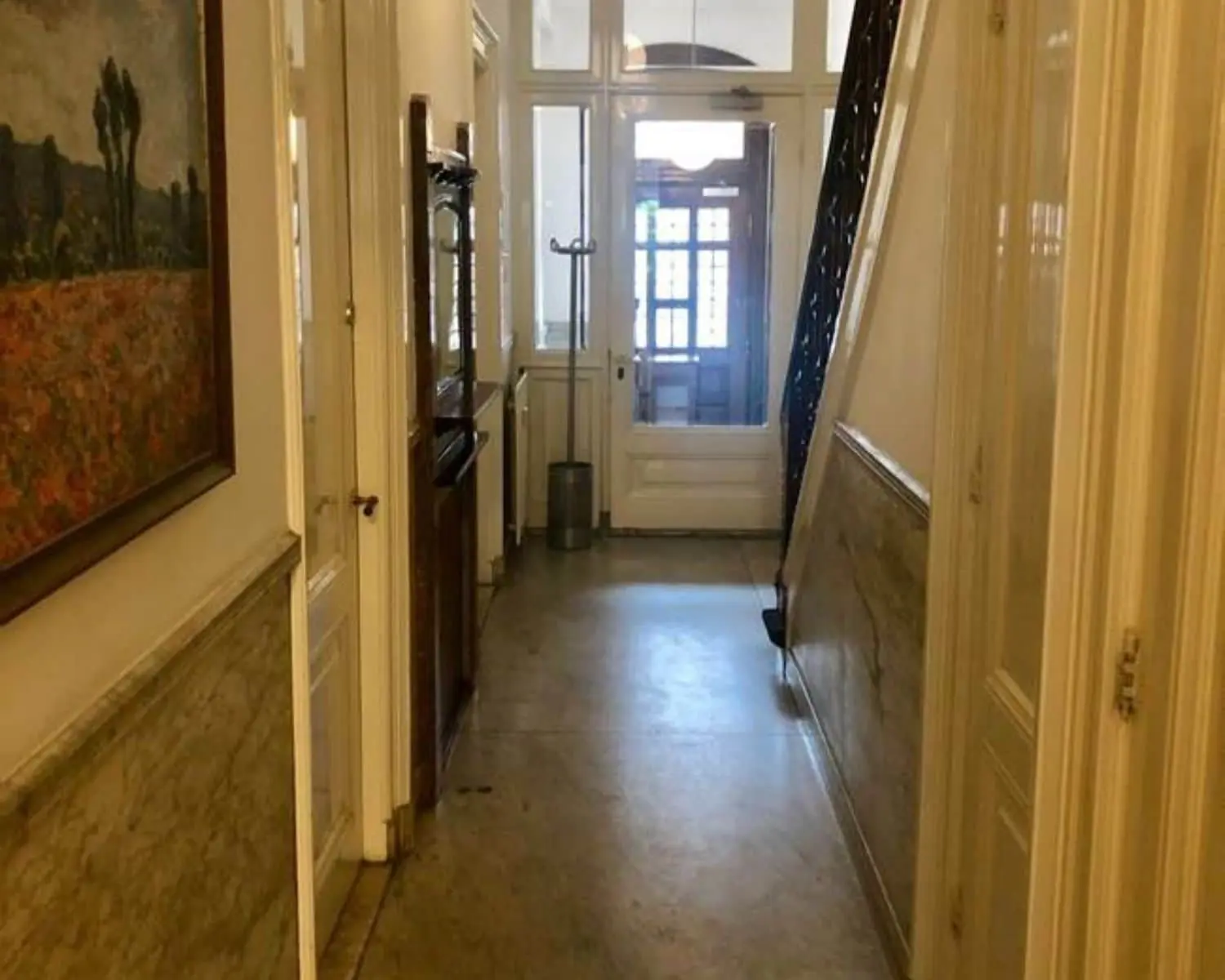 Smalle, klassieke hal met marmeren lambrisering, een schilderij aan de muur en een trap aan de rechterzijde.