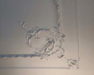 Wit plafond met sierlijke, barokke stucdecoratie in een hoekpatroon.
