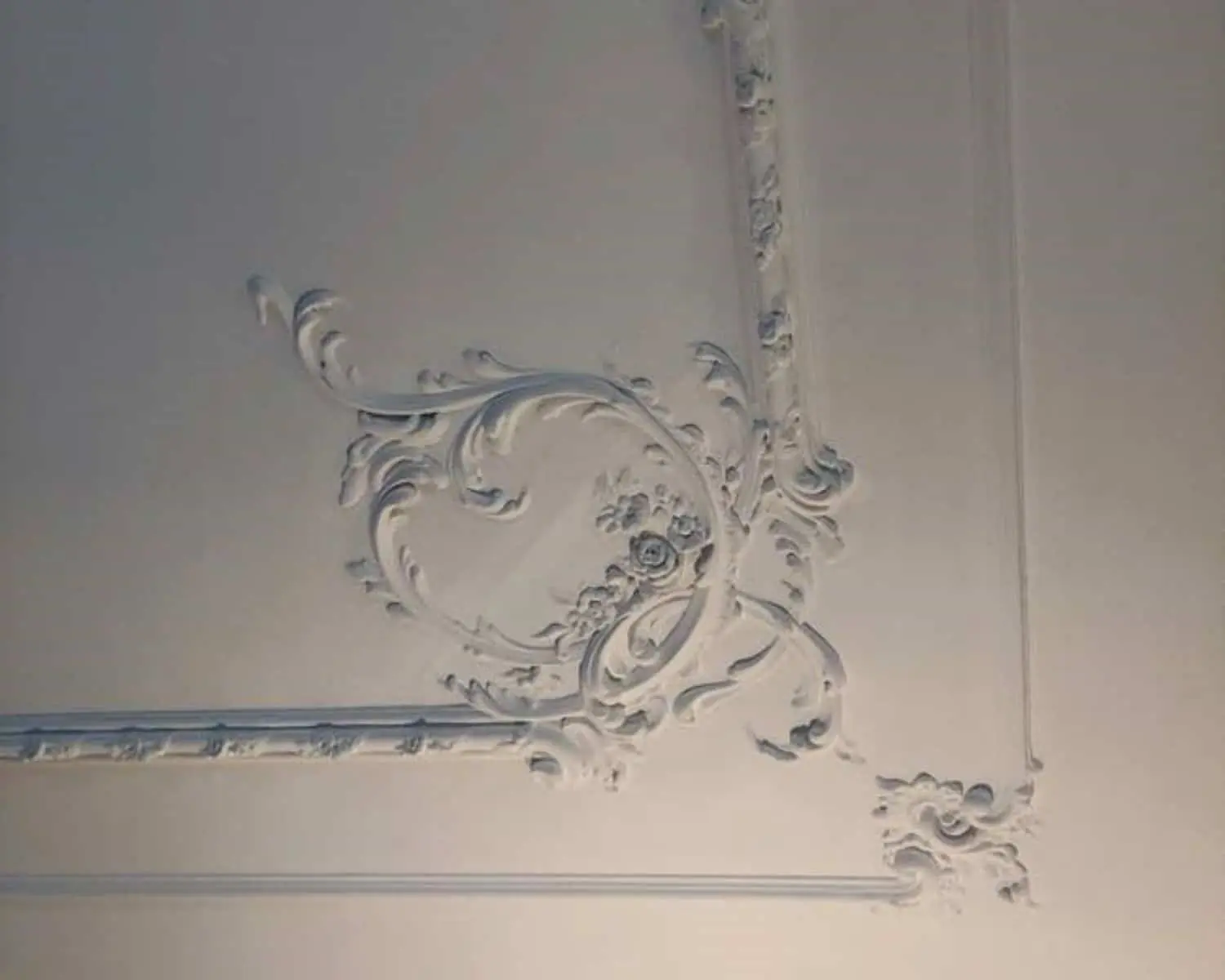 Wit plafond met sierlijke, barokke stucdecoratie in een hoekpatroon.