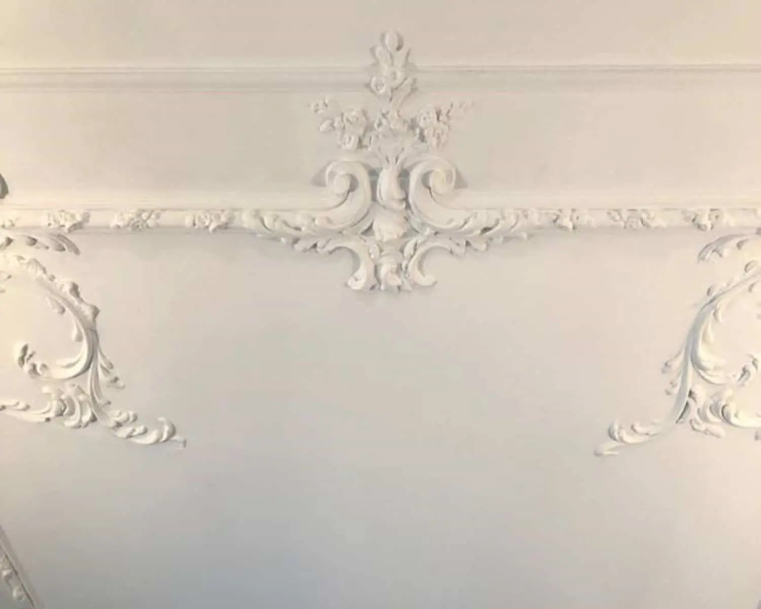 Wit plafond met sierlijke, klassieke ornamenten in reliëf.