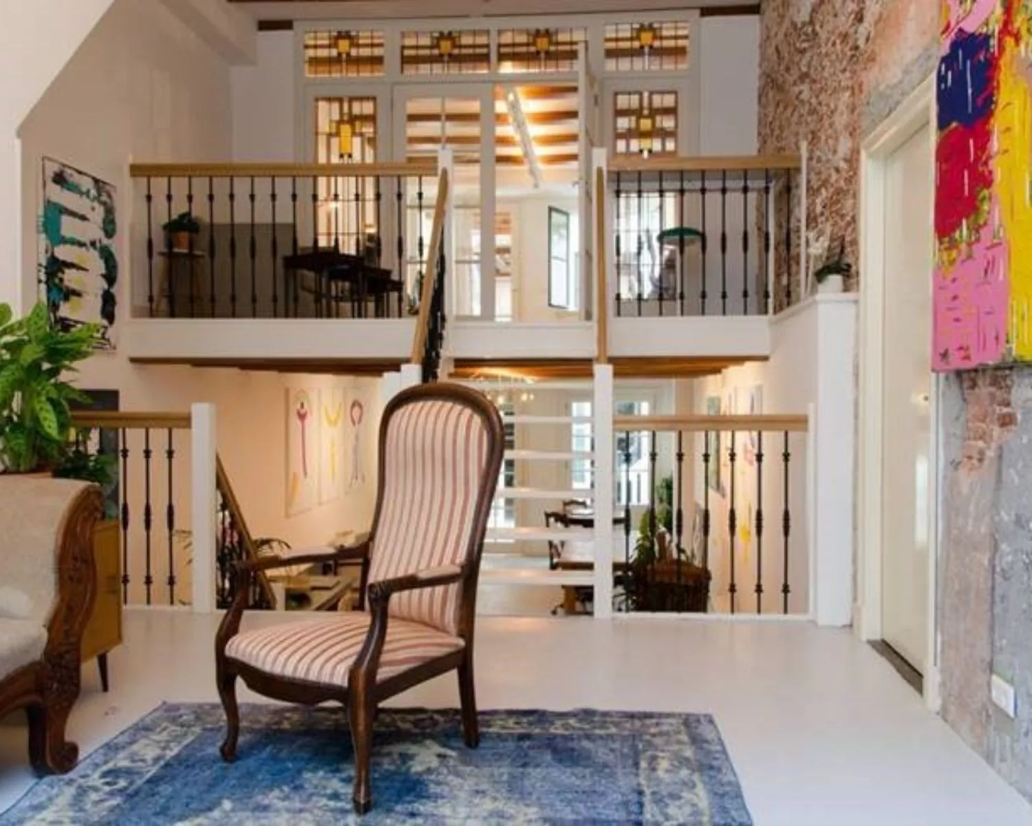 Stijlvol ingerichte woonkamer met een hoge rugleuningstoel op een blauw vloerkleed en zicht op een open vide met sierlijke balustrades.