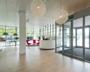Moderne en lichte ontvangsthal met glazen schuifdeuren, een receptiebalie en rode loungefauteuils.